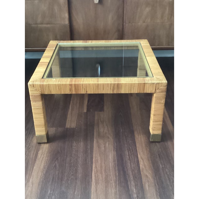 A stylish vintage wicker coffee table featuring a finely wrapped rattan frame accented by brass-capped feet and a brand-...