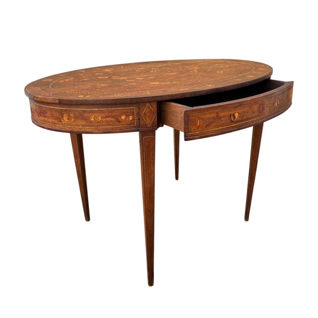 Elegant oval side table crafted in wood and richly decorated with fine marquetry, inspired by the Louis XVI style. The...