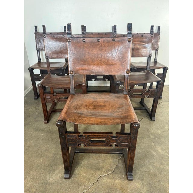 A striking set of six Spanish Revival armchairs crafted from richly patinated hardwood and fitted with hand-tooled leather...