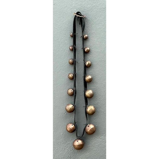This vintage strand of sleigh bells is a long, graduated line of round brass bells mounted in pairs along a flat black...