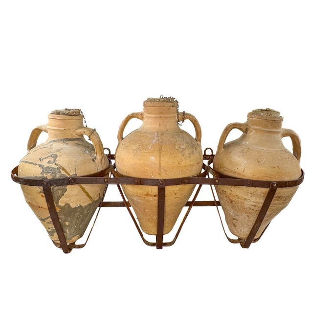 Three Spanish terra cotta Oil Jars on metal rack that hangs on a wall.