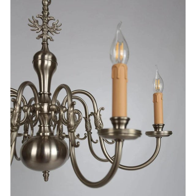 Eight-armed chandelier made of white brass decorated with an eagle and fish on top. The chandelier has undergone a...
