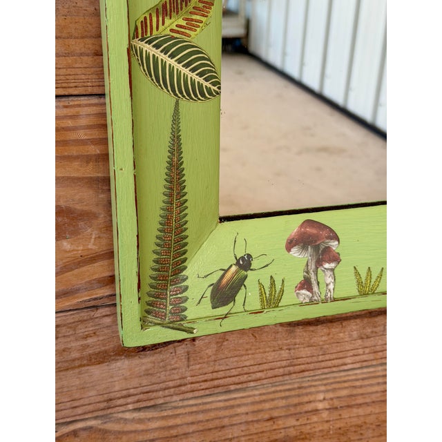 A charming vintage wooden wall mirror featuring a soft green painted frame adorned with colorful tropical birds,...