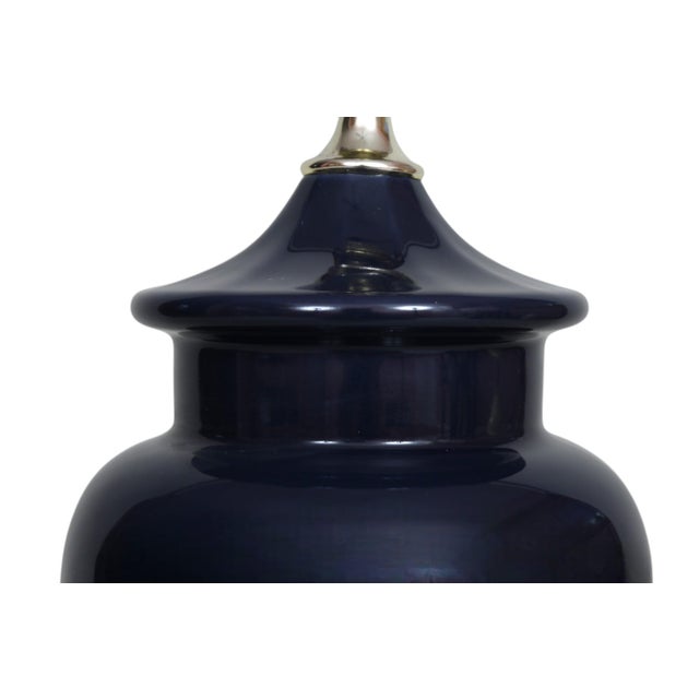 A deep blue ceramic table lamp. The round ceramic vase is ginger jar shaped, and sits on a round beveled wooden base with...