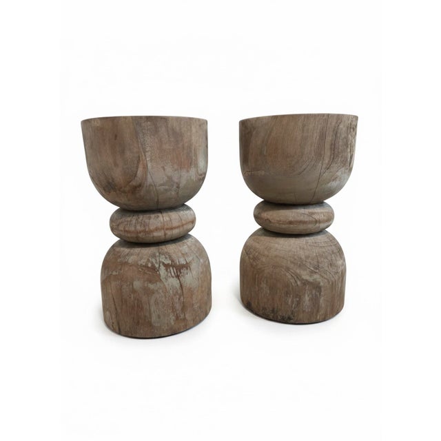 The hourglass form has been executed in teak a thousand times. This pair gets it right. The weathered surface — silvered...