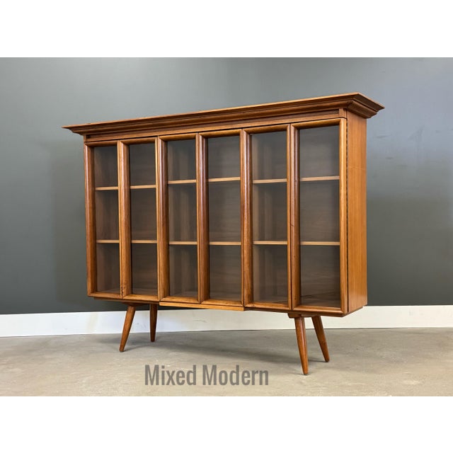 A mid century modern walnut bookcase with three doors, walnut shelves and long canted legs. Excellent condition. Circa...