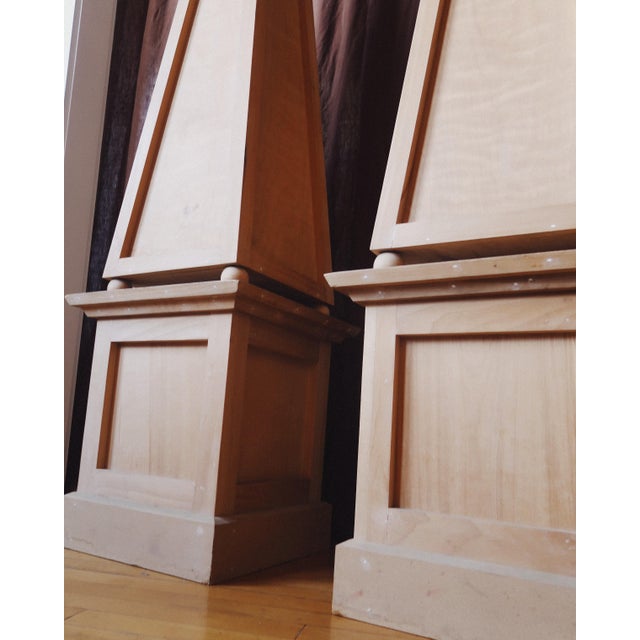 A pair of monumental wooden obelisks with paneled plinth bases and tall, tapered upper forms. At 75 inches in height,...