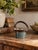 A vintage handmade studio pottery basket featuring a sculptural arched handle, softly flared rim, and rounded stoneware...