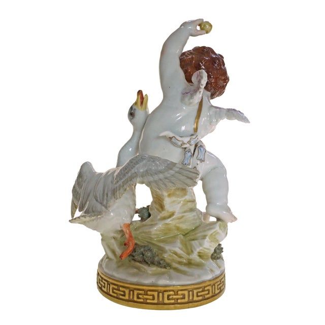 A large and beautifully detailed porcelain group depicting a red-haired cherub holding an apple aloft, playfully teasing a...