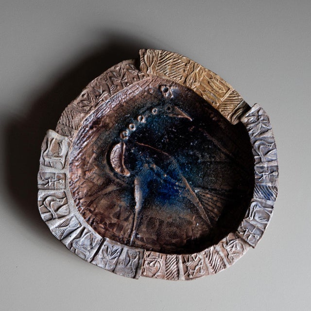 Italian ceramic plate with a wide rim, decorated with scenes in prehistoric forms and a stylized peacock bird in the well....