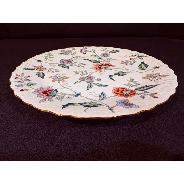 This distinctive porcelain plate has a colorful floral motif and features a scalloped and embossed rim with gold trim.