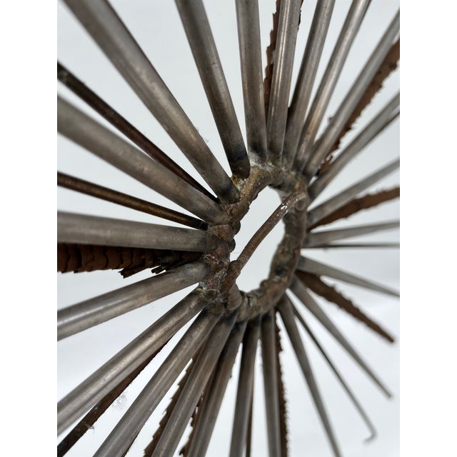 A single vintage round metal industrial style sunburst sculpture with grey metal and twisted rusted tin accents.