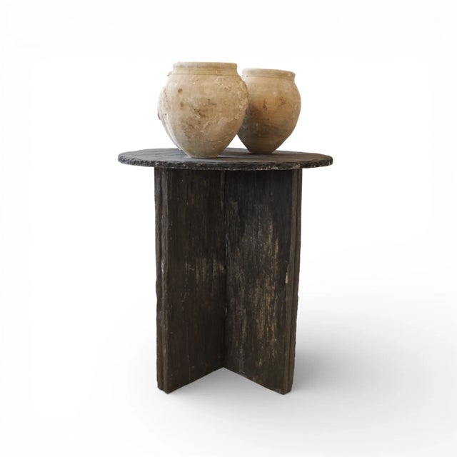 A round slate table anchored by a sculptural X-shaped base, combining natural texture with architectural presence. The...