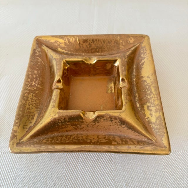 This Mid-Century Modern Stangl Pottery Granada Gold ashtray showcases a bold, sculptural square form with softly raised...