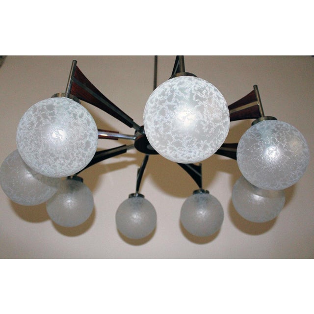 This living room chandelier in chrome-plated brass features teak details and spherical diffusers made of etched crystal...