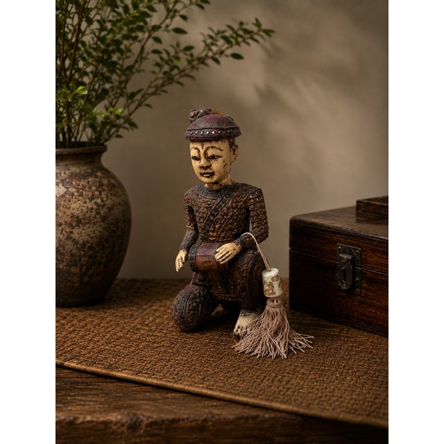 This finely detailed hand-carved Chinese wooden figural sculpture depicts a seated musician holding a small drum, rendered...