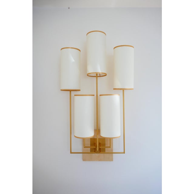 A wall light in patinated gold metal, with a sycamore base. The lampshades are white fabric with a gold trim. It hangs...