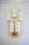 A wall light in patinated gold metal, with a sycamore base. The lampshades are white fabric with a gold trim. It hangs...