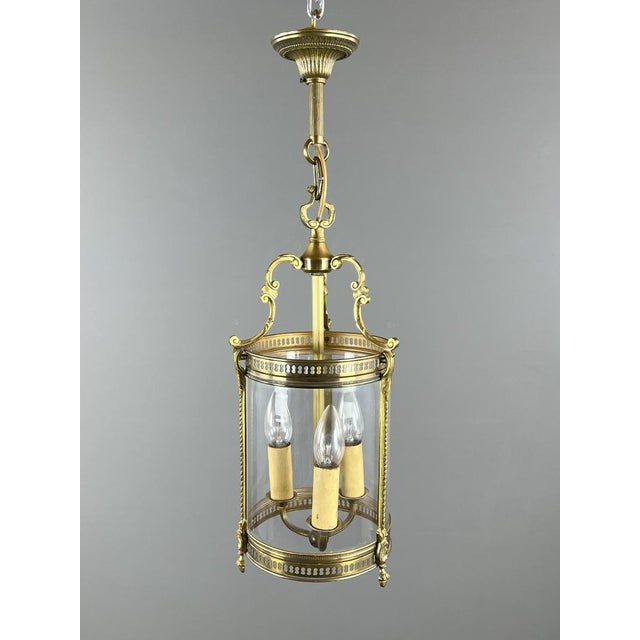 An elegant cylindrical hanging lantern in bronze and glass. The finely crafted frame features openwork decoration and...