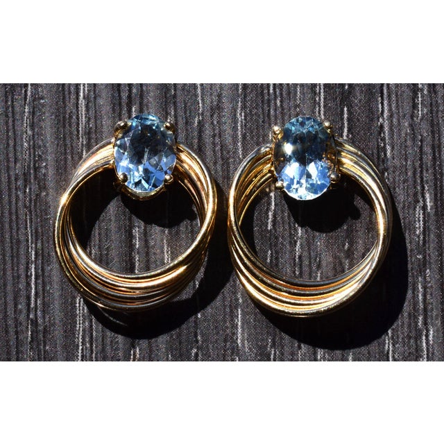 The West Hartley: Circular Earrings set with Aquamarine in Yellow Gold. The earrings features a single oval brilliant cut...