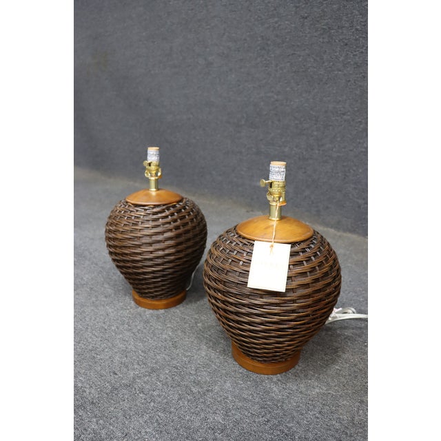 Pair of Ralph Lauren table lamps with woven wicker bases and wood accents. Rounded form with a warm brown finish. Classic,...