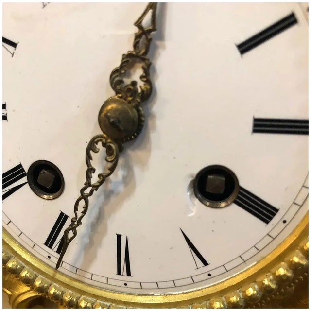 This antique French mantel clock is topped by the figure a young girl standing by a pedestal table with an open box. MAKER...