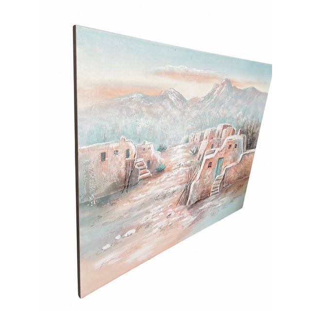 A tranquil Southwestern landscape featuring adobe-style buildings nestled beneath a sweeping mountain range. Soft peach,...