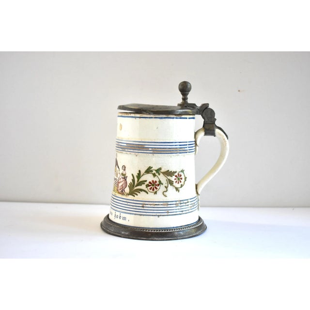 An antique, c. 1800-1815 German or Thuringian pewter-mounted tin-glazed, hand-painted faience stein or tankard, featuring...