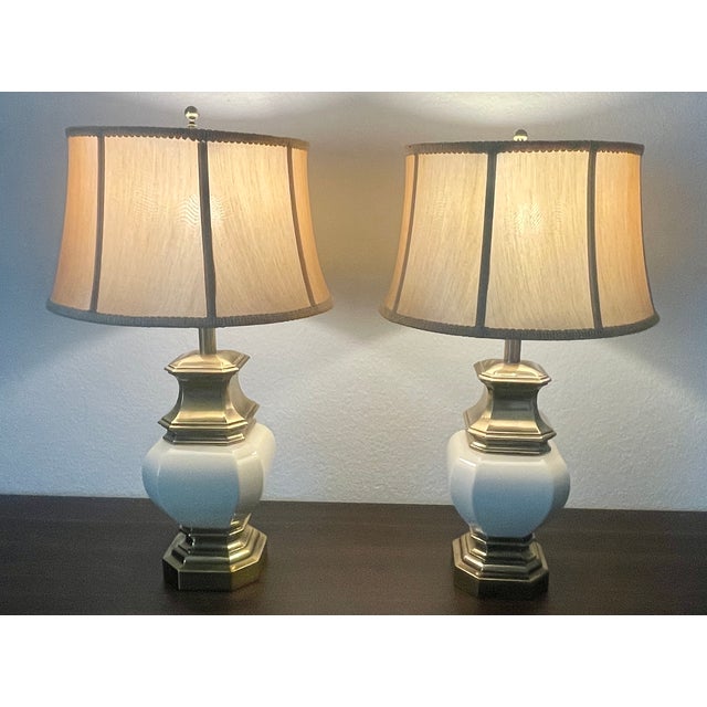 A rare and elegant pair in the Hollywood Regency or Traditional style. Brass base and top frame the bulbous, porcelain...