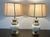 A rare and elegant pair in the Hollywood Regency or Traditional style. Brass base and top frame the bulbous, porcelain...