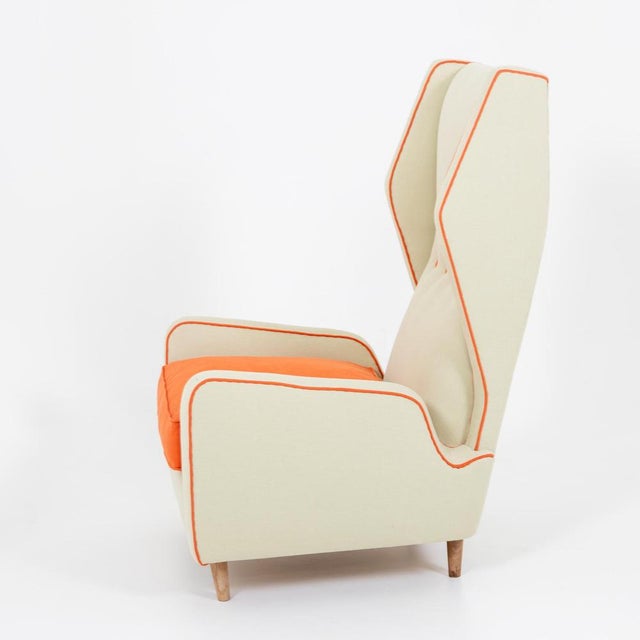 Italian mid-century lounge chair with high backrest and armrests. The armchair has light-colored upholstery and is...