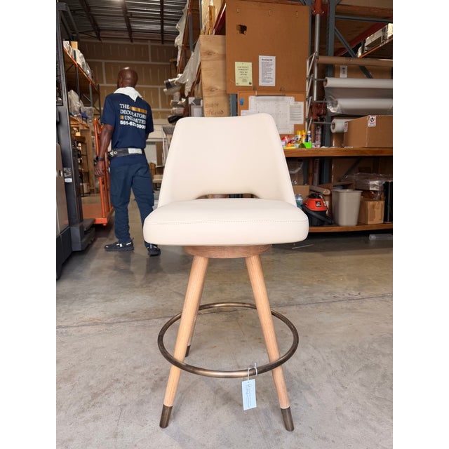 Contemporary counter stool featuring a clean, minimalist silhouette upholstered in smooth cream leather. The gently curved...