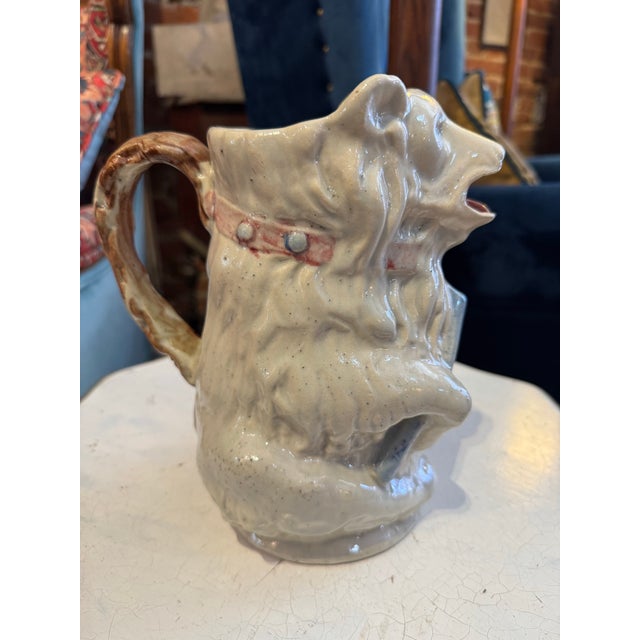 Antique French majolica pottery pitcher in the form of a blue-eyed, white bear holding a blue stick, wearing a studded...