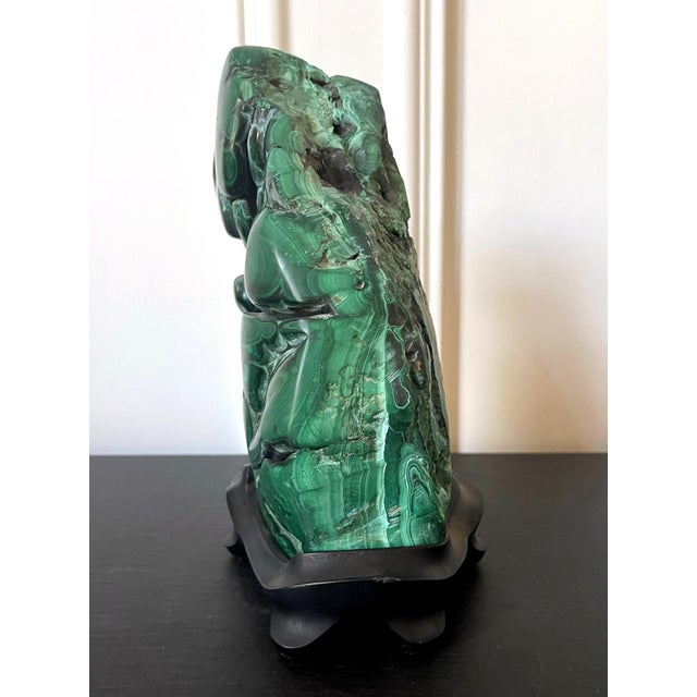 A malachite rock specimen with intense green and black colors fitted on a wood stand and displayed as a <a...