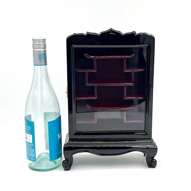 Vintage glass door display cabinet features a classic Chinoiserie design with stepped interior shelving and a glossy...