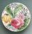 A colorful Italian ceramic cake stand decorated with a large pink rose, purple daisies, a yellow tulip & blue forget me...