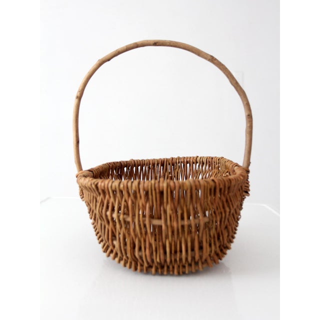 A vintage handwoven wicker basket with a sculptural, scalloped form and an arched handle, crafted in natural fibers with a...