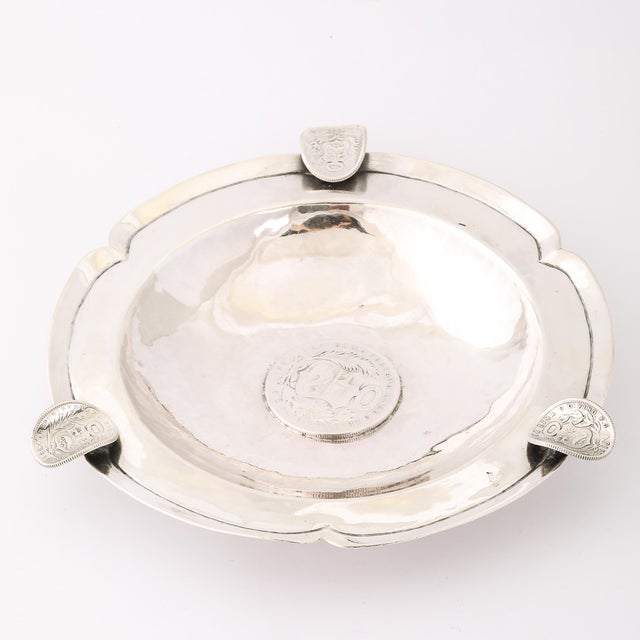 This Art Deco Hand-Hammered Ashtray W/Inset Sculptural Coins, crafted in Peru in the 20th century from .900 sterling...