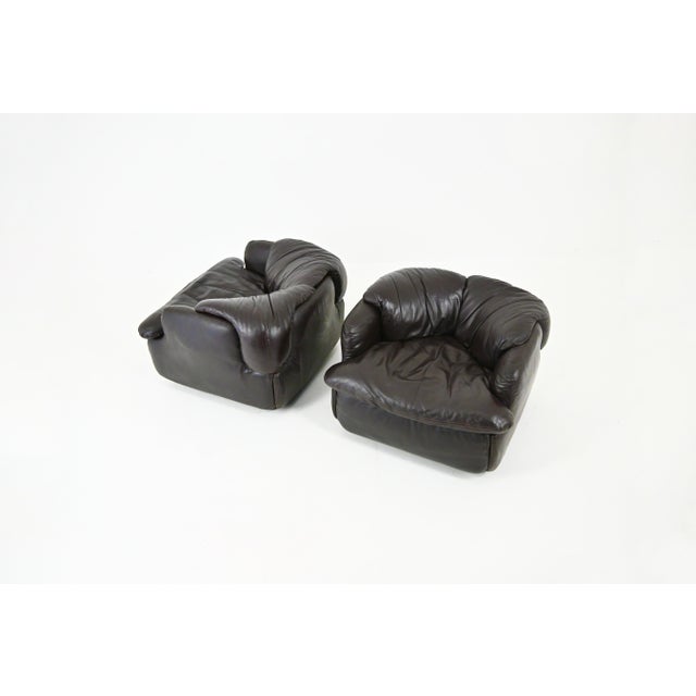 Pair of dark brown leather armchairs with plastic legs. Stamped Saporiti. Seat height 41 cm. Wear consistent with age and...