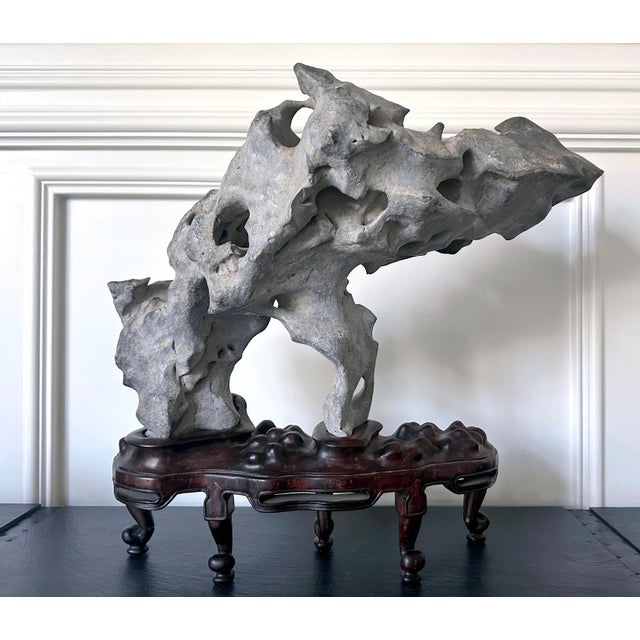 A stunning Taihu scholar stone in an unusual horizonal balanced form perched on a custom wood stand. The stone, in a...
