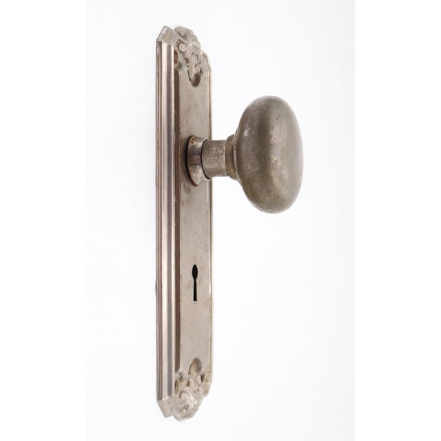 Art Deco style dummy door knob set with a round brushed nickel brass knob and a pressed steel back plate with foliate...