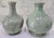 A vintage pair of Thai celadon ceramic vases featuring a soft sage-green finish, glossy crackle glaze, and two distinct,...