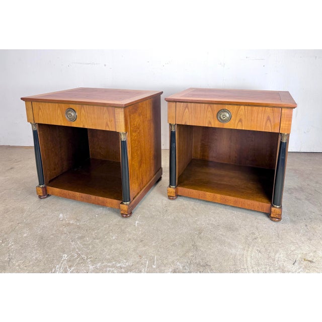 A delightful pair of Neoclassical / French Empire Baker Furniture single-drawer nightstands in two-tone cherry wood,...