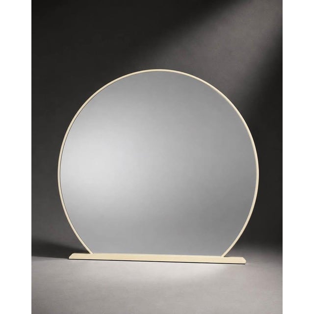 A large round mirror with a soft cream-colored frame and a clean sculptural base. The rounded silhouette and neutral...