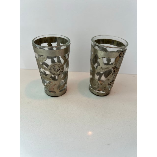 Set of two shot glasses with a silver overlay. The overlay has etched leaves and a woven design.