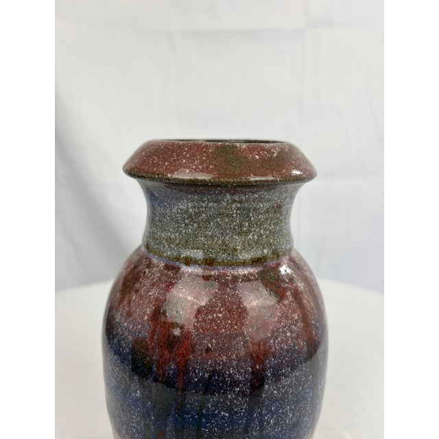 A signed studio pottery vase featuring a rich drip glaze in layered tones of purple, blue, and burgundy over a warm sienna...