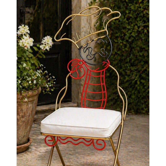 A charming pair of whimsical chef-themed metal folding chairs, thoughtfully refreshed and styled with plush ivory...