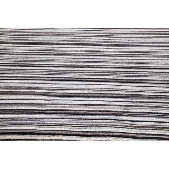 A stunning modern hand-woven wool rug boasting an Ivory color field and exquisite stripe design detailing with brown and...