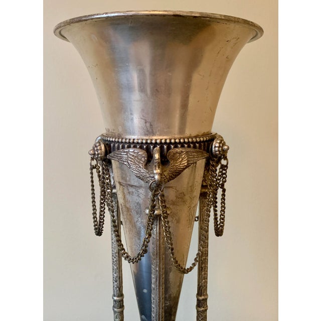 A stunning vintage silver plated neoclassical style vase. The stand rests on three paw feet, a stylized base, another set...
