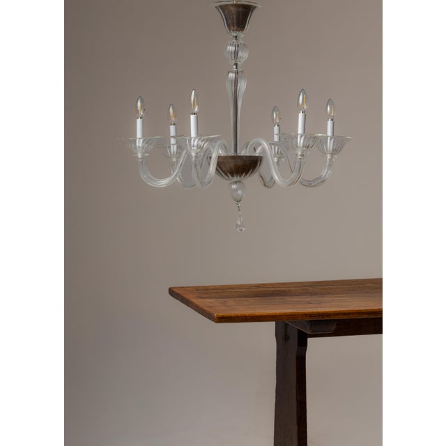 A handblown clear glass chandelier in the Venetian tradition, featuring six scrolling S-curved arms with ruffled bobeches,...